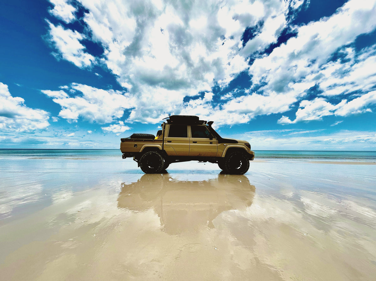Sandy coloured 79 series landcruiser on the beach with reflection